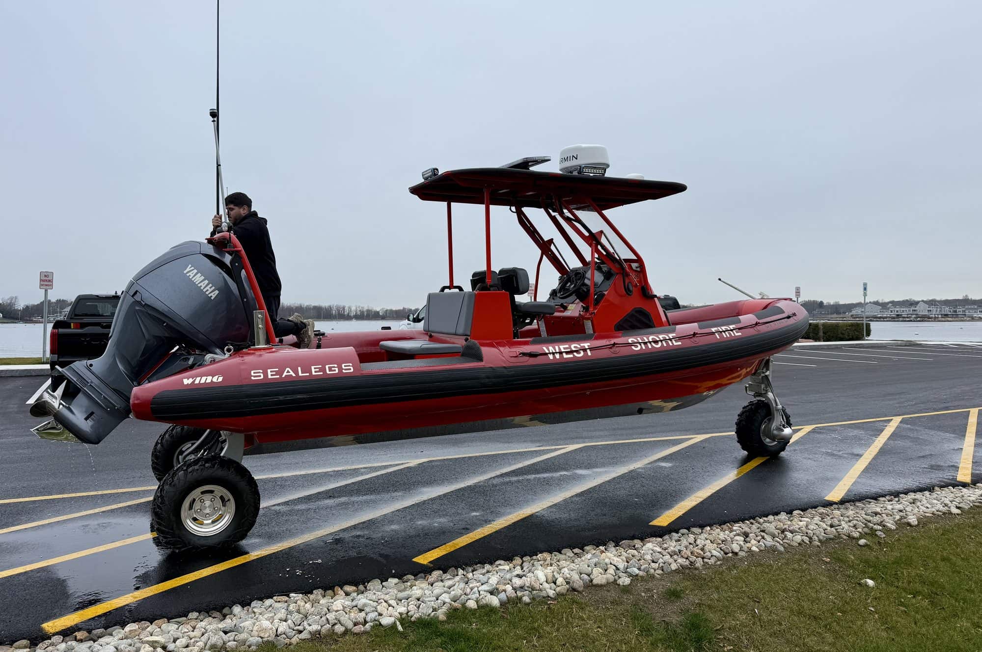 A fire and rescue Sealegs RIB in red livery driving on its wheels across a waterfront parking area